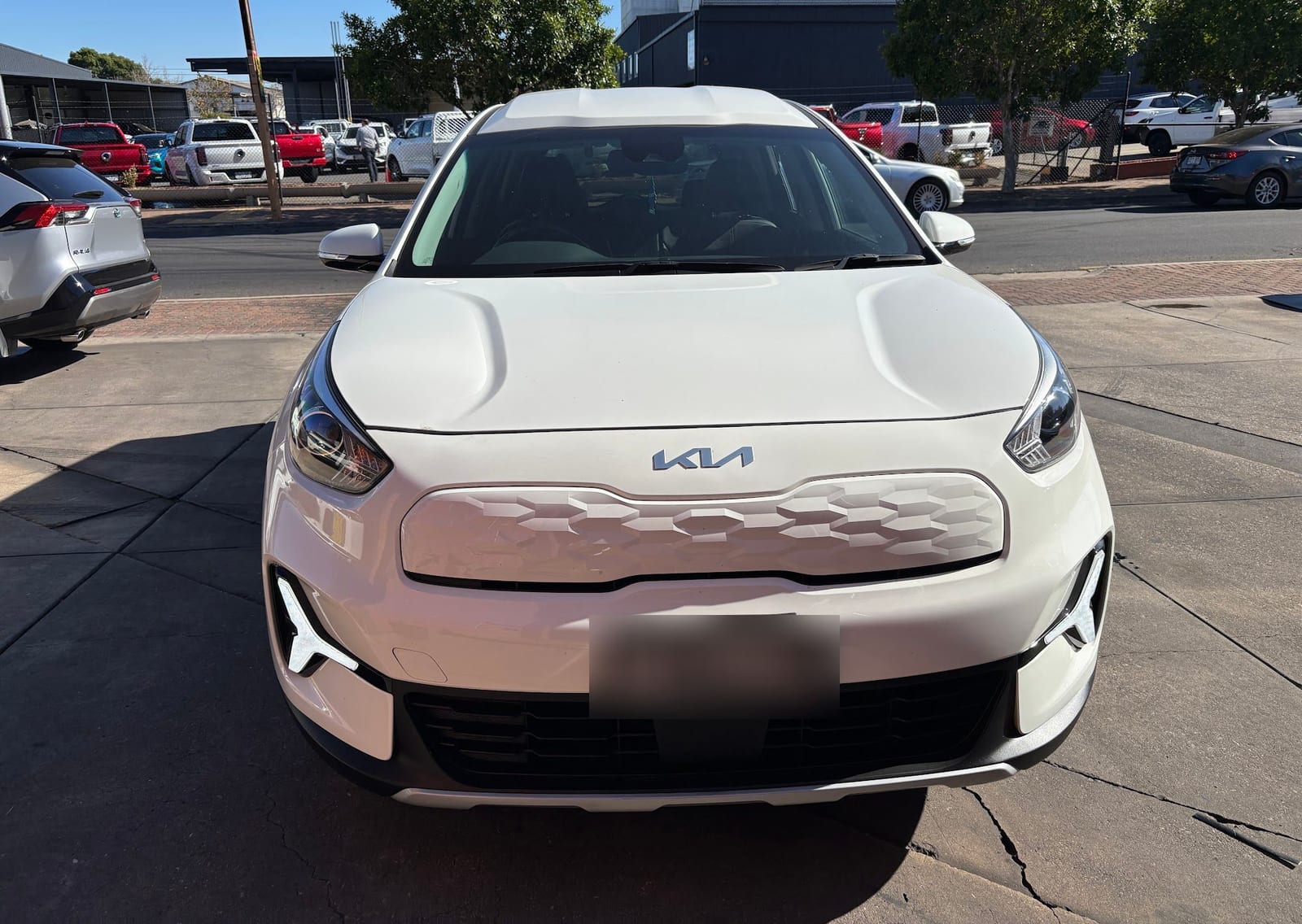 A white Kia SUV seen from the front, with its number plate blurred